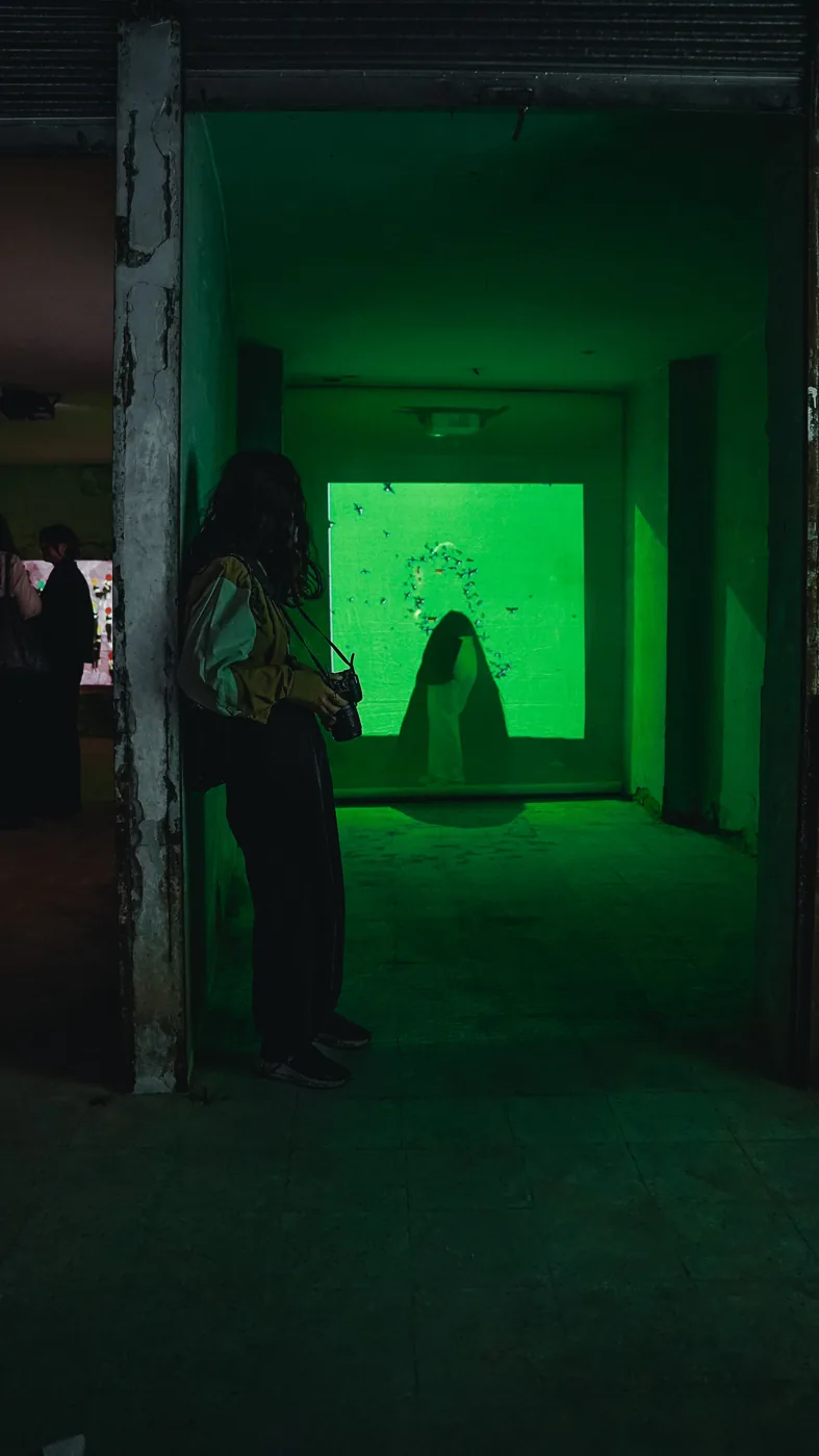 Green light fills an exhibition room around a visitor’s silhouette.